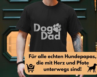 May include: Black t-shirt with the text "Dog Dad" in white, featuring a paw print design. The shirt also has a text in German that says "Für alle echten Hundepapas, die mit Herz und Pfote unterwegs sind!"