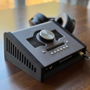 May include: A silver and black audio interface with a large knob and multiple buttons. The interface is labeled "Universal Audio".