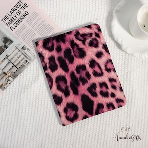 Könnte beinhalten: Ein Notizbuch oder Journal mit einem rosa-schwarzen Leopardenmuster. Der Einband zeigt ein auffälliges Muster aus dunklen Flecken auf rosa Grund. Die daneben liegende Zeitschrift trägt den Text "THE LARGEST FAMILY OF THE FLOWERING".