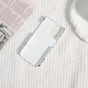 Puede incluir: Una funda de tel&eacute;fono blanca con un borde azul claro y un patr&oacute;n de peque&ntilde;os corazones rojos. La funda tiene recortes para la c&aacute;mara y los botones, y est&aacute; dise&ntilde;ada para proteger el tel&eacute;fono.