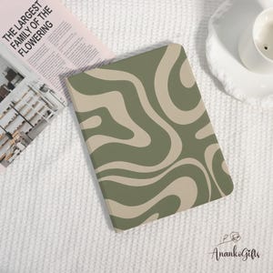 May include: A notebook with a green and beige wavy pattern. The notebook is on a white textured surface, next to a magazine with the text "THE LARGEST FAMILY OF THE FLOWERING". A white teacup and saucer are also visible.