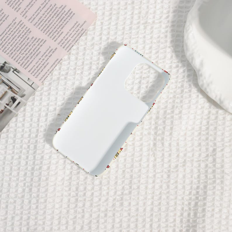 May include: White phone case with a colorful pattern around the edges. The case has cutouts for the camera and buttons. The pattern includes small, colorful shapes and designs. The case is on a white textured surface.