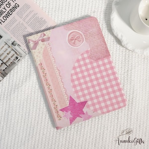 May include: A rectangular notebook with a collage-style cover featuring shades of pink. The design includes a pink gingham pattern, a wax seal graphic with a bow, a floral border, and three glittery pink stars layered over a script background.