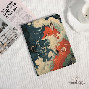 May include: A notebook with a stylized illustration of a red fox with white and cream accents against a dark teal background. The fox is surrounded by swirling white clouds. The text "THE LARGEST FAMILY OF THE FLOWERING" is visible on a magazine.