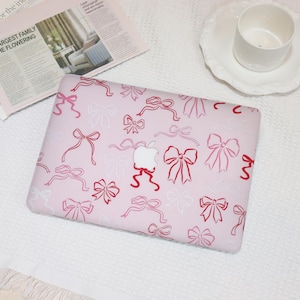 May include: Pink laptop case with a white and red bow pattern. The Apple logo is visible on the case.
