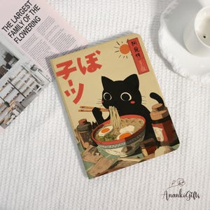 May include: A beige notebook featuring a black cat illustration enjoying ramen noodles. The cover includes Japanese text and a red sun. The notebook is surrounded by condiments and a magazine.