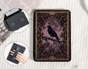 Pode incluir: Capa preta para e-reader com um desenho de corvo empoleirado num galho dentro de uma moldura dourada. O fundo é roxo escuro com detalhes dourados. Um suporte e uma alça de mão pretos separados também são visíveis.