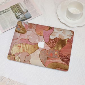 May include: A laptop skin featuring an abstract collage of pink, peach, and cream organic shapes accented with metallic gold foil textures and intricate floral patterns. The design covers the lid, leaving the white Apple logo visible in the center.