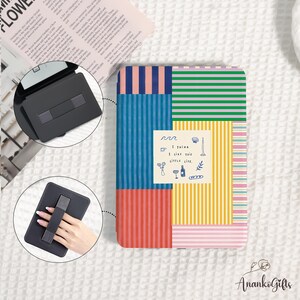 May include: A colorful tablet case with a patchwork design of vertical and horizontal stripes in various colors, including blue, pink, green, and yellow. A small square sticker with the text "I think I like this little life" is on the case. A black tablet stand is also visible.