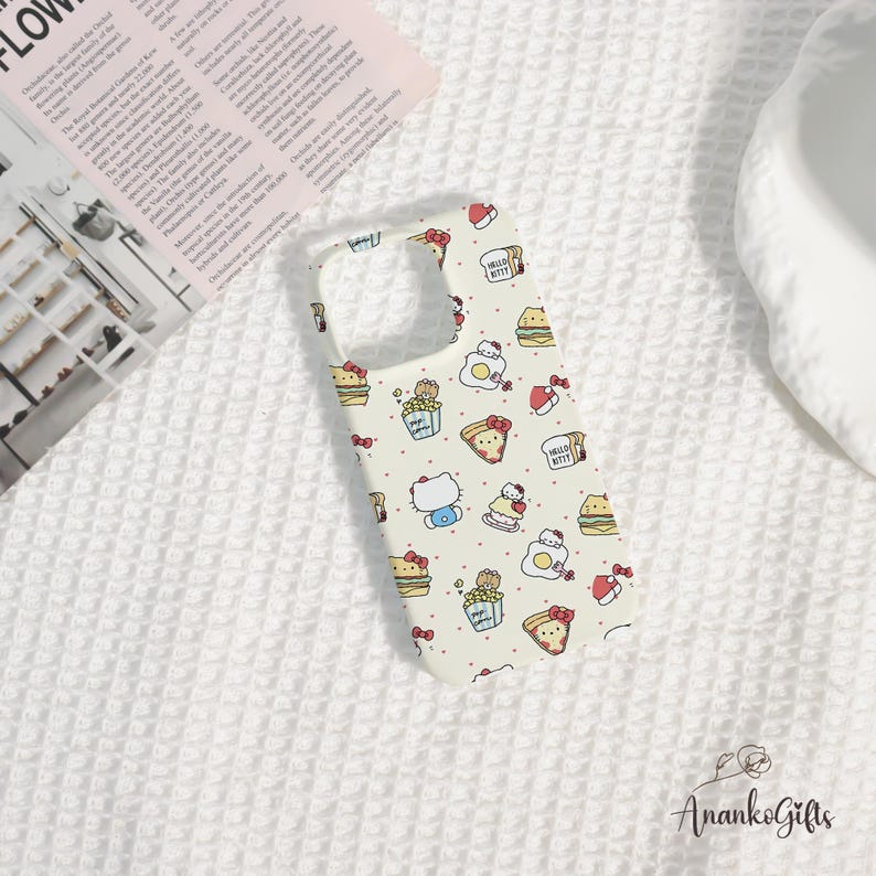 May include: A cream-colored phone case featuring a repeating pattern of Hello Kitty characters, food items, and red bows. The case has cutouts for the camera and buttons. The words "Hello Kitty" are printed on some of the food items.