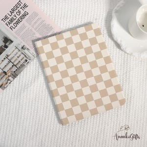 May include: A beige and white checkered pattern notebook. The notebook is rectangular with rounded corners. The text "THE LARGEST FAMILY OF THE FLOWERING" is visible on a magazine in the background.