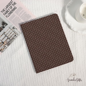 Könnte beinhalten: Ein braunes Notizbuch mit weißem Polka-Dot-Muster. Das Notizbuch liegt auf einer weißen, strukturierten Oberfläche neben einer Zeitschrift mit dem Text "THE LARGEST FAMILY OF THE FLOWERING".