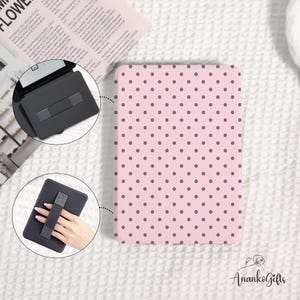 May include: Pink tablet case with a brown polka dot pattern. The case has a built-in hand strap for easy holding. A black tablet stand is also shown. The brand name "AnankoGifts" is visible.