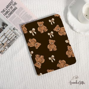 May include: A brown notebook cover with a repeating pattern of teddy bears and bows. The bears are light brown with dark brown accents, and the bows are cream-coloured. The text "THE LARGEST FAMILY OF THE FLOWERING" is visible on a magazine.