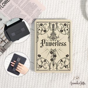 May include: A cream-colored e-reader case featuring a black decorative illustration of a dagger surrounded by floral vines and the word Powerless in the center. Two circular insets show the black interior with a strap and the back with a hand strap.