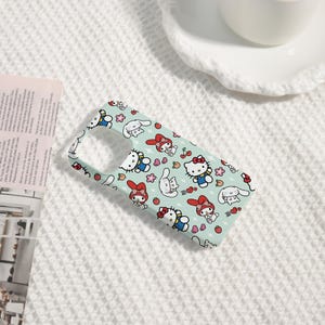 Puede incluir: Funda de tel&eacute;fono azul claro con un patr&oacute;n repetido de personajes de dibujos animados, incluyendo un gato con un lazo rojo, un conejo blanco, flores y fresas. La funda est&aacute; dise&ntilde;ada para un smartphone.
