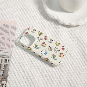 May include: A light-colored phone case featuring a repeating pattern of Hello Kitty characters, food items, and red bows. The case has a cutout for the camera and buttons. The background is a white, textured surface.