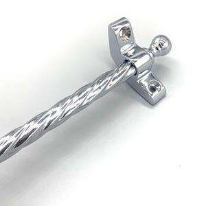 May include: A polished chrome window stay with a decorative twisted rod. The stay features a ball finial and mounting plates with screw holes, designed for secure installation. The hardware is made of shiny metal.
