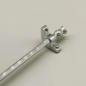 May include: A polished chrome curtain rod with a decorative pineapple-shaped finial. The rod has a ribbed design and is attached to a rectangular bracket with screw holes. The finial adds a touch of elegance.