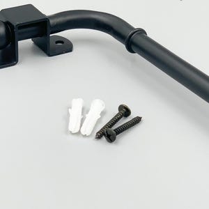 Könnte beinhalten: Schwarzer Türgriff aus Metall mit abgerundetem Ende und einem kugelförmigen Knauf. Der Griff ist an einer quadratischen Basis mit zwei Montageöffnungen befestigt. Der Griff wird mit zwei Schrauben und zwei weißen Kunststoffdübeln geliefert.