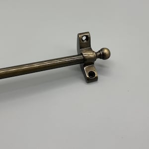 May include: A brushed antique brass curtain rod with a finial. The rod is approximately 36 inches long and has a square bracket with two screw holes.