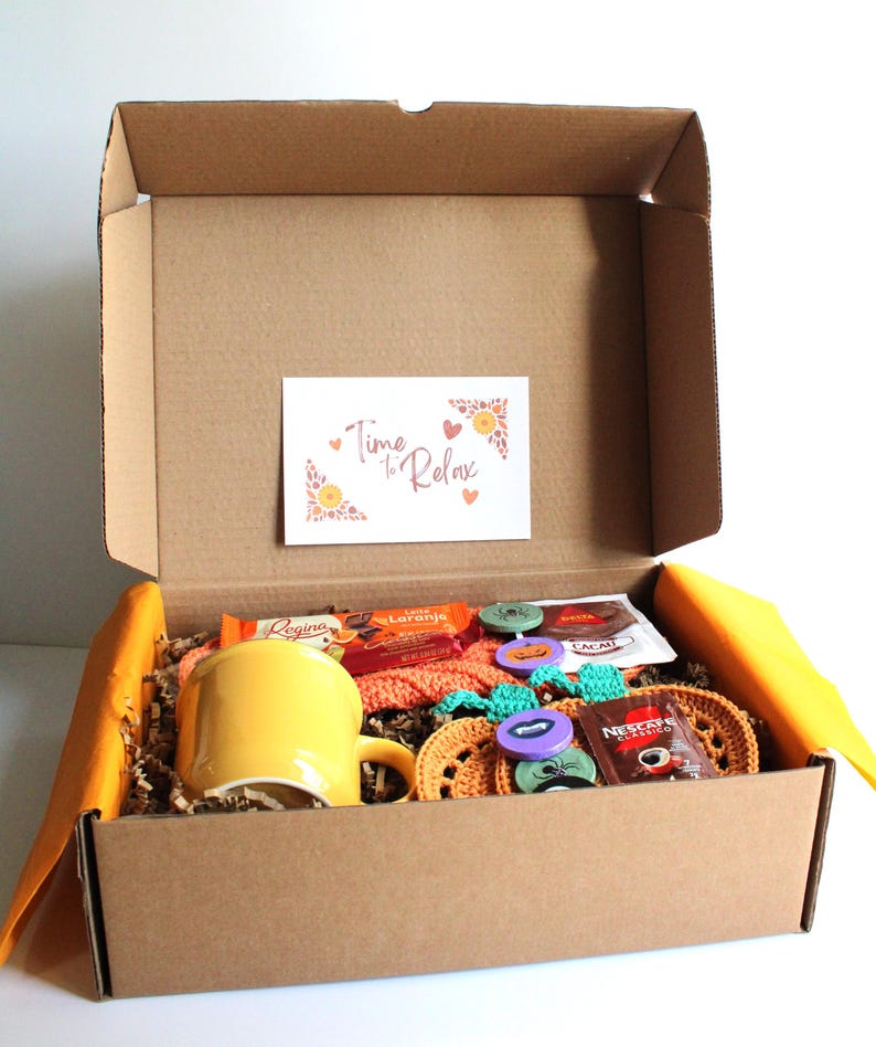 May include: A cardboard box filled with relaxation items. Inside, a yellow mug, crochet coasters, and a small card that reads "Time to Relax". The box also contains snacks and coffee packets.