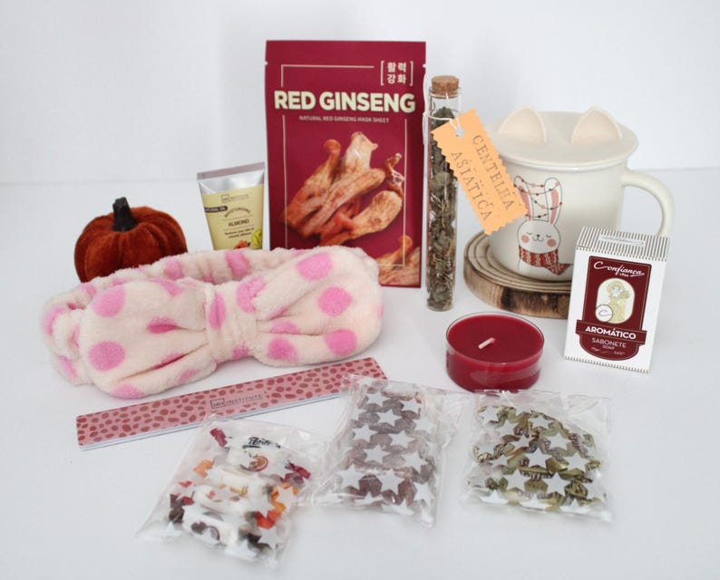 May include: A collection of self-care items, including a plush pink polka-dot headband, a red candle, a mug with a bunny design, and a package of Red Ginseng face mask. Other items include a nail file and small bags of decorative items.
