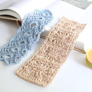 May include: Two handmade crochet bookmarks in the image. One is light blue, the other is tan. The bookmarks are placed on an open book. A small candle and tea bags are also in the image.