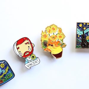 May include: Four enamel pins featuring art-inspired designs: a bottle containing a starry night scene, a stylized portrait of a man with a bandage labeled VINCENT, a vase of yellow sunflowers, and a rectangular pin depicting a swirling night sky.
