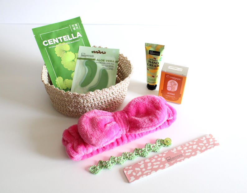 May include: A collection of beauty and self-care products, including a pink headband, a woven basket with face masks, hand cream, and a nail file. The face masks are labeled "Centella" and "Aloe Vera". The nail file has a pink and white pattern.