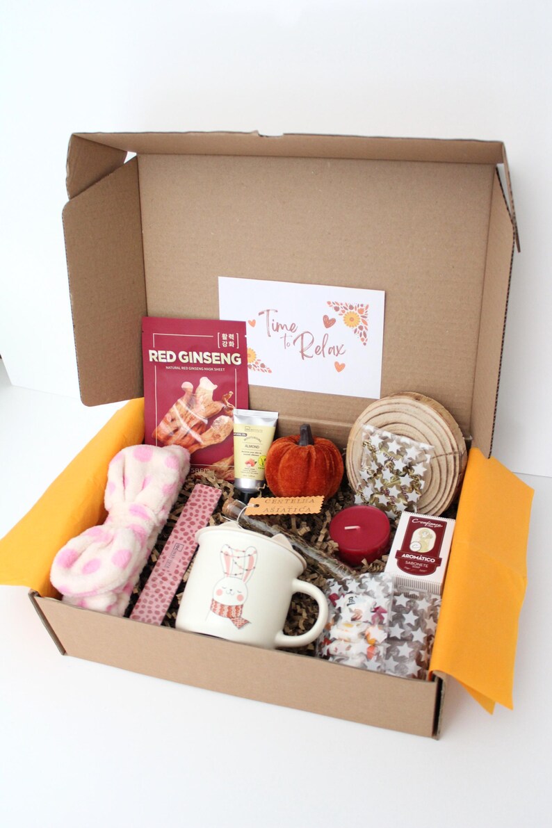 May include: A gift box filled with self-care items. Includes a mug with a bunny design, a red ginseng face mask, a small orange pumpkin, a candle, and a headband. The box also contains a card that says "Time to Relax".