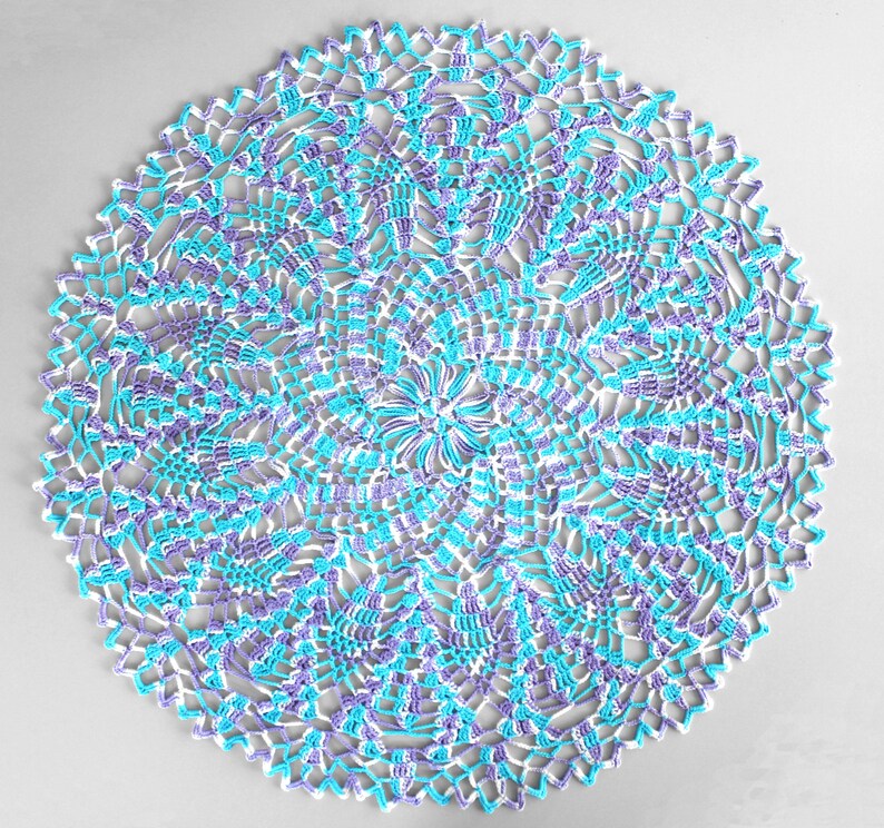 Pu&ograve; includere: Un centrino rotondo fatto a mano, con un motivo floreale. Il centrino &egrave; lavorato all'uncinetto con filato bianco, azzurro e viola. I bordi hanno un design smerlato. Questo articolo decorativo &egrave; adatto per l'arredamento della casa.