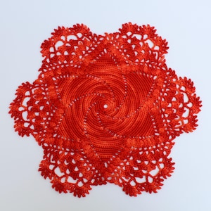 May include: A handmade, bright red crocheted doily with a spiral center and a scalloped edge. The doily is circular and features an open, lacy design. This decorative item is suitable for various home decor uses.
