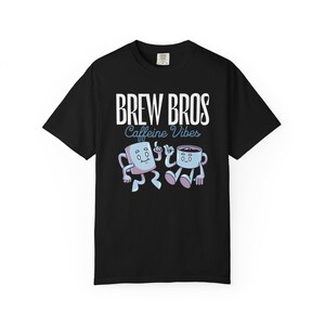 May include: Black t-shirt with the text "BREW BROS Caffeine Vibes" in white and light blue. The shirt features cartoon illustrations of a marshmallow and a coffee cup with arms and legs, in light blue and purple.