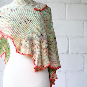 May include: A light green and white knitted shawl with a pink crocheted border. The shawl is draped over a white mannequin.