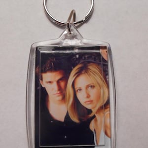 May include: A clear plastic keyring with a photo of two people. The photo shows a man and a woman. The man is wearing a black shirt and the woman is wearing a white shirt. The keyring is attached to a silver ring.