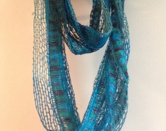 May include: A turquoise blue crocheted scarf with a beaded trim. The scarf is hanging on a black hanger against a white background.