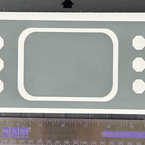 May include: A gray bandage-shaped sticker with a white border and white octagonal shapes. The center has a rectangular shape with rounded corners. A ruler is at the bottom.