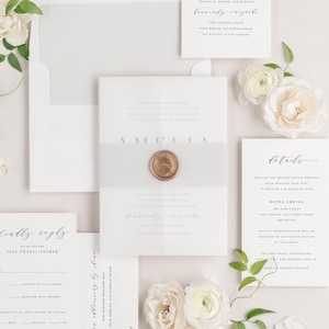 Amelia invitation flat lay with soft gray envelope liner, soft gray belly band, translucent vellum jacket, and gold wax seal.