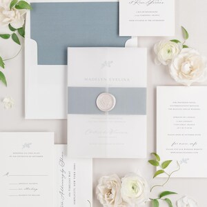 May include: A wedding invitation suite with a blue and white color scheme. The invitation features a wax seal and the text "Madelyn Evelina". The RSVP card includes the text "Please RSVP by the sixteenth of September". The details card includes the text "456 Timeless Way, Simplicity, New York 10061".