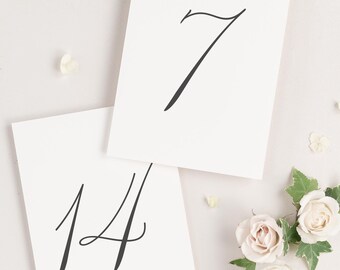 May include: Two white cards with black calligraphy numbers, 7 and 14, on a white background with white flowers and green leaves.
