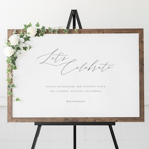 May include: A wooden sign with a white background and black text that reads "Let's Celebrate" with the names Sienna Rutherford and Anthony Klein, the location The Landsby, Solvang, California, and the hashtag #loveisklein.