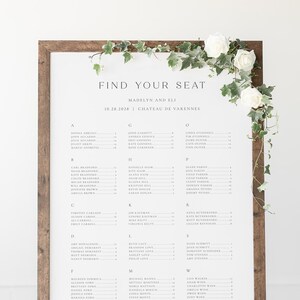 May include: A white seating chart with a brown wooden frame. The chart is titled "Find Your Seat" with the names of guests listed alphabetically by last name. The chart is for a wedding at Chateau de Varennes on October 28, 2028.