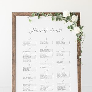 May include: A white wedding seating chart with a wooden frame. The chart is titled "Your seat awaits" and lists the names of guests and their assigned tables. The bottom of the chart reads "Sienna and Anthony".
