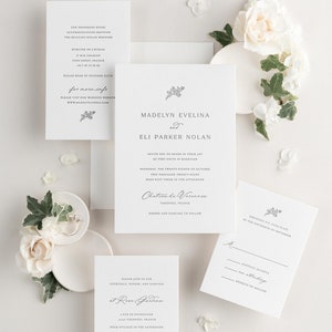 May include: A white wedding invitation suite with a floral design. The invitation features the names Madelyn Evelina and Eli Parker Nolan, the wedding date, and the location. The RSVP card includes the text "RSVP by the sixteenth of September".