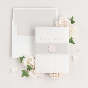 Poppy save the dates with a feather belly band, translucent vellum jacket, and pearl wax seal.