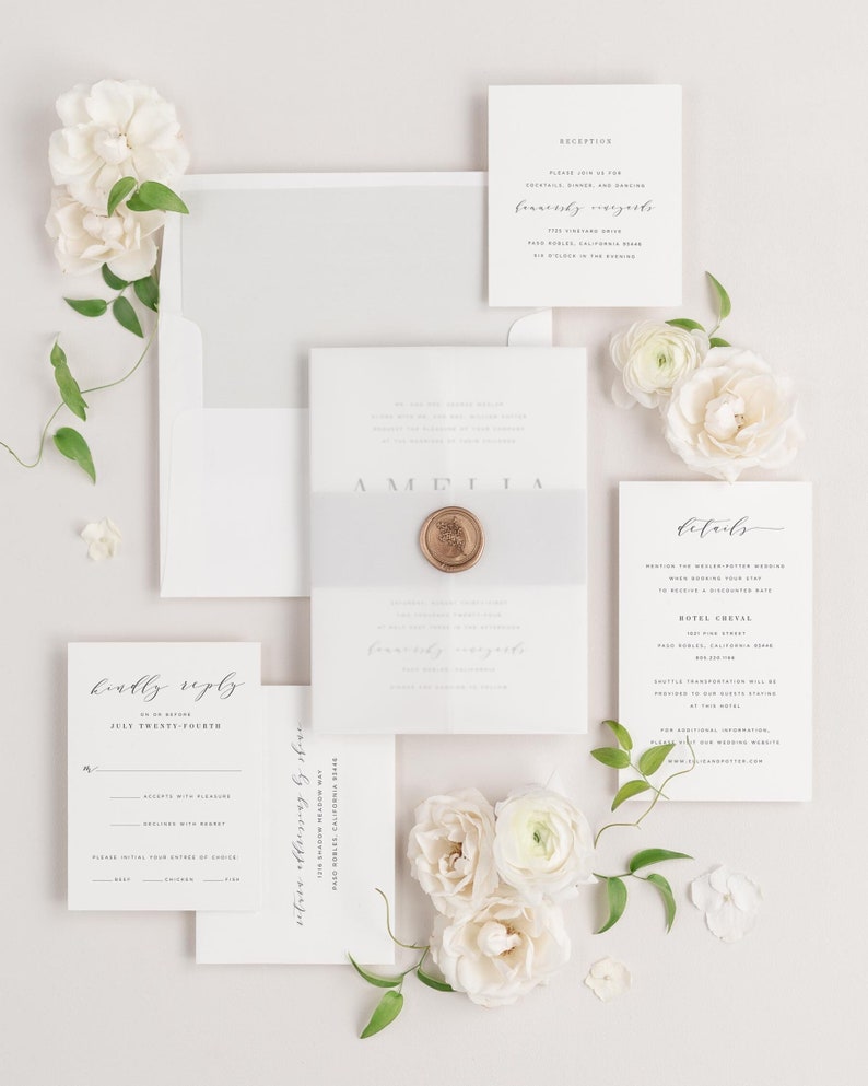 Amelia invitation flat lay with soft gray envelope liner, soft gray belly band, translucent vellum jacket, and gold wax seal.