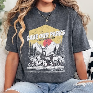 May include: A gray t-shirt with a vintage-style graphic design featuring a forest scene with animals and the text "Save Our Parks Resist-Defend-Protect".
