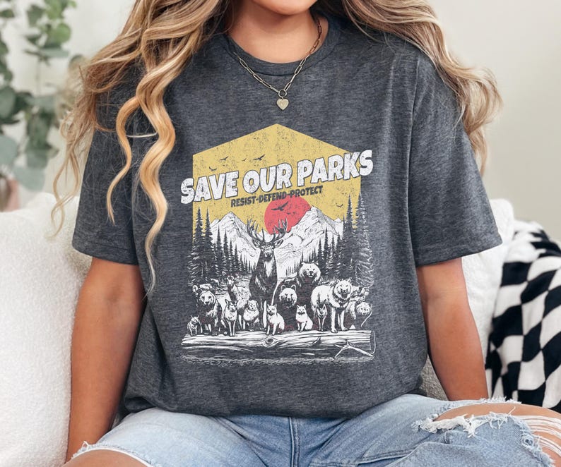 May include: A gray t-shirt with a vintage-style graphic design featuring a forest scene with animals and the text "Save Our Parks Resist-Defend-Protect".