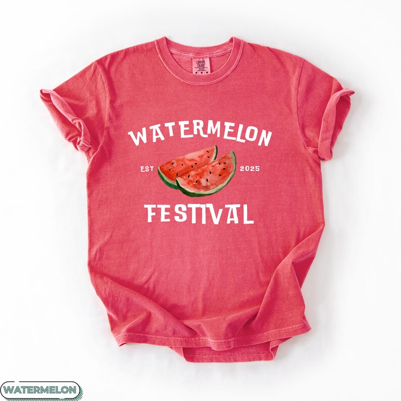 Pu&ograve; includere: Una maglietta rossa con le parole "WATERMELON FESTIVAL" in bianco. La maglietta presenta un'illustrazione ad acquerello di due fette di anguria. Il testo "EST 2025" &egrave; anch'esso stampato.